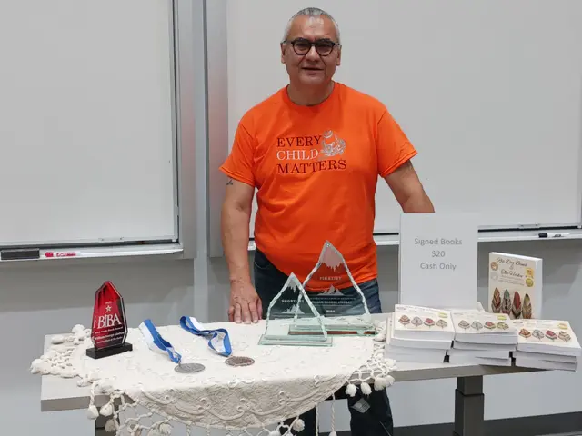 William in an Every Child Matters shirt behind a table of signed books and award trophies