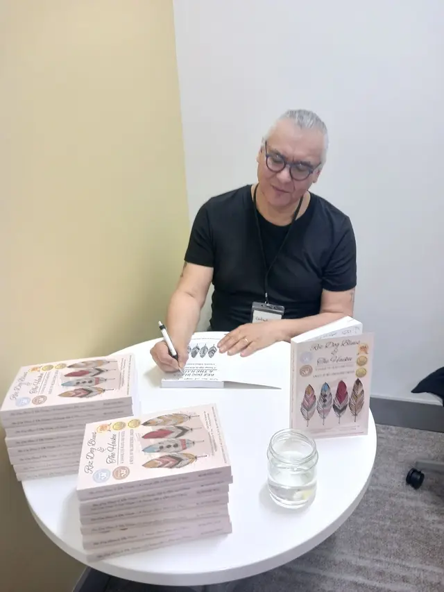 William signing books at a round table with stacks of the novel